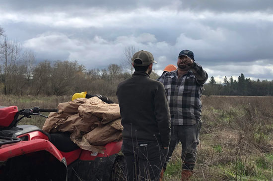 one person directs another at a planting site on an overcast day